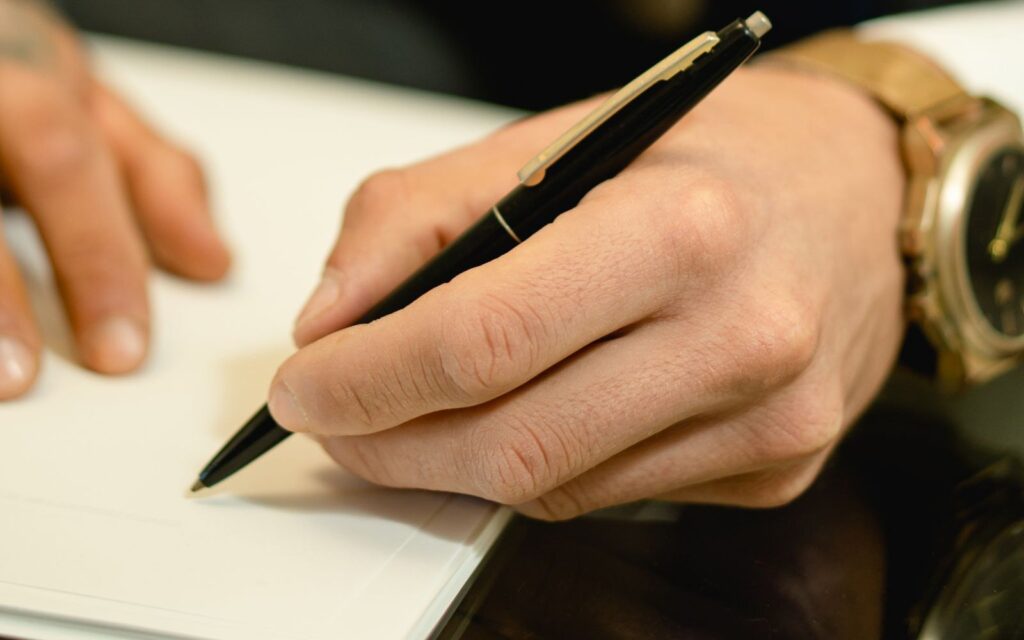 Gros plan sur une main qui signe un acte au stylo, sur un bureau